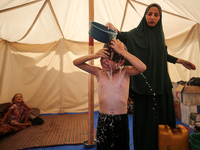 A displaced Palestinian mother is showering her child amid a heat wave inside a tent at a temporary camp in Deir el-Balah in the central Gaz...