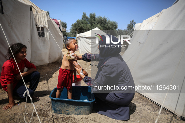 A displaced Palestinian mother is showering her child amid a heat wave outside a tent at a temporary camp in Deir el-Balah in the central Ga...