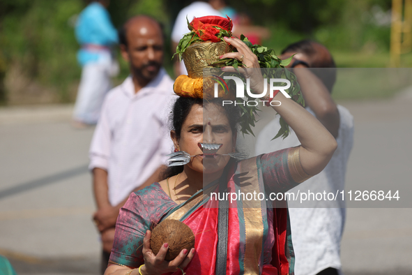 A Tamil Hindu woman is carrying a pot on her head filled with milk and honey, with a facial skewer, as devotees are taking part in the chari...