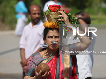 A Tamil Hindu woman is carrying a pot on her head filled with milk and honey, with a facial skewer, as devotees are taking part in the chari...