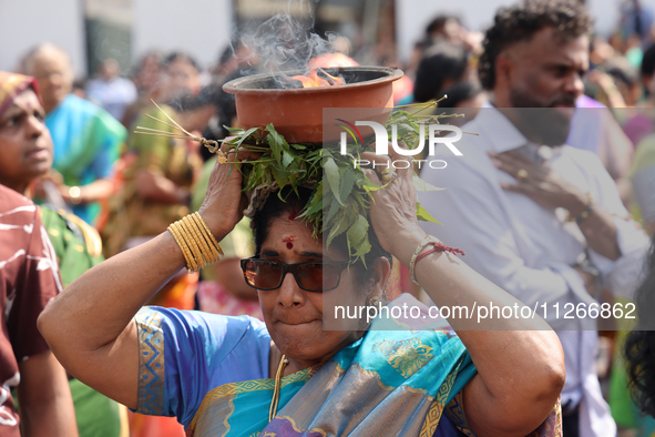 A woman is carrying a clay pot with flaming camphor on her head as Tamil Hindu devotees are taking part in the chariot procession (ther) dur...