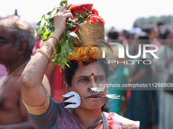 A Tamil Hindu woman is carrying a pot on her head filled with milk and honey, with a facial skewer, as devotees are taking part in the chari...