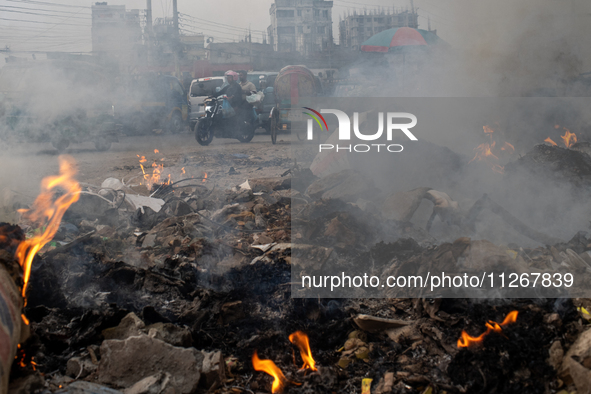 People are moving past burning garbage and plastic trash beside a busy road in Dhaka, Bangladesh, on May 23, 2024. Dhaka's air quality is be...