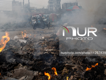 People are moving past burning garbage and plastic trash beside a busy road in Dhaka, Bangladesh, on May 23, 2024. Dhaka's air quality is be...