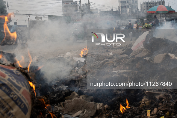 People are moving past burning garbage and plastic trash beside a busy road in Dhaka, Bangladesh, on May 23, 2024. Dhaka's air quality is be...