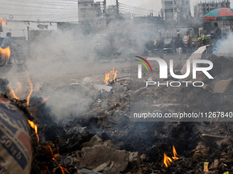 People are moving past burning garbage and plastic trash beside a busy road in Dhaka, Bangladesh, on May 23, 2024. Dhaka's air quality is be...