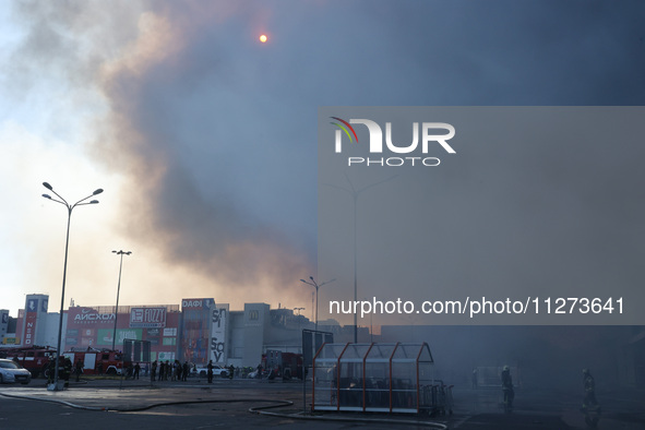 The sun is being seen through smoke rising over an Epicentr K construction supermarket hit with two Russian glide bombs in Kharkiv, Ukraine,...