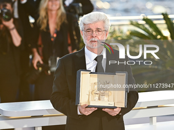 George Lucas is posing with the Honorary Palme D'Or Award during the Palme D'Or Winners Photocall at the 77th annual Cannes Film Festival at...