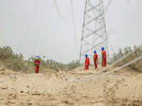 Construction workers are erecting a power grid at the Bazhou-Tieganlik-Ruoqiang 750 kV transmission line project site in Korla, China, on Ma...