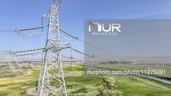 Construction workers are erecting a power grid at a height at the Bazhou-Tieganlik-Ruoqiang 750 kV transmission line project site in Korla,...