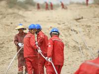 Construction workers are erecting a power grid at the Bazhou-Tieganlik-Ruoqiang 750 kV transmission line project site in Korla, China, on Ma...