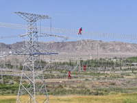 Construction workers are erecting a power grid at a height at the Bazhou-Tieganlik-Ruoqiang 750 kV transmission line project site in Korla,...
