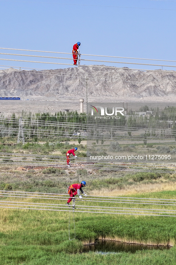 Construction workers are erecting a power grid at a height at the Bazhou-Tieganlik-Ruoqiang 750 kV transmission line project site in Korla,...