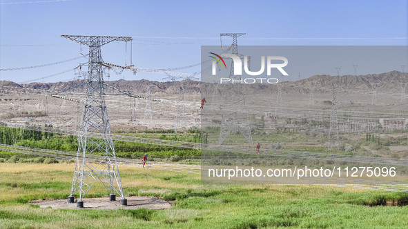 Construction workers are erecting a power grid at a height at the Bazhou-Tieganlik-Ruoqiang 750 kV transmission line project site in Korla,...