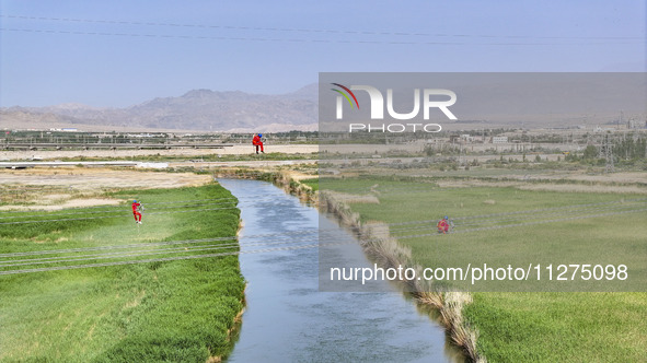 Construction workers are erecting a power grid at a height at the Bazhou-Tieganlik-Ruoqiang 750 kV transmission line project site in Korla,...