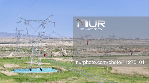 Construction workers are erecting a power grid at a height at the Bazhou-Tieganlik-Ruoqiang 750 kV transmission line project site in Korla,...