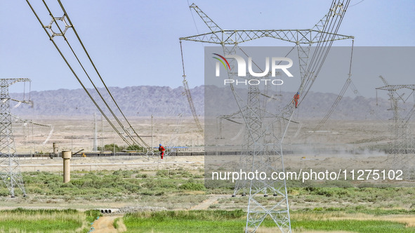 Construction workers are erecting a power grid at a height at the Bazhou-Tieganlik-Ruoqiang 750 kV transmission line project site in Korla,...