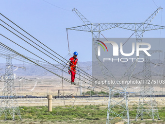 Construction workers are erecting a power grid at a height at the Bazhou-Tieganlik-Ruoqiang 750 kV transmission line project site in Korla,...