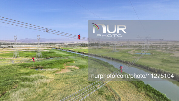 Construction workers are erecting a power grid at a height at the Bazhou-Tieganlik-Ruoqiang 750 kV transmission line project site in Korla,...