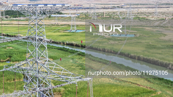 Construction workers are erecting a power grid at a height at the Bazhou-Tieganlik-Ruoqiang 750 kV transmission line project site in Korla,...