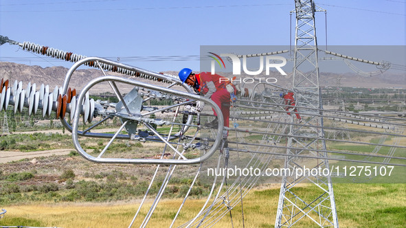 Construction workers are erecting a power grid at a height at the Bazhou-Tieganlik-Ruoqiang 750 kV transmission line project site in Korla,...