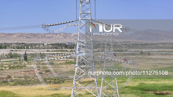 Construction workers are erecting a power grid at a height at the Bazhou-Tieganlik-Ruoqiang 750 kV transmission line project site in Korla,...