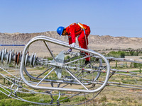 Construction workers are erecting a power grid at a height at the Bazhou-Tieganlik-Ruoqiang 750 kV transmission line project site in Korla,...