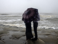 A couple is trying to escape the rain by holding an umbrella at Kuakata Sea Beach in southern Bangladesh on May 26, 2024, as Cyclone Remal n...