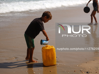 A Palestinian boy is washing kitchenware on the beach in Deir el-Balah, central Gaza Strip, on May 26, 2024, amid the ongoing conflict betwe...