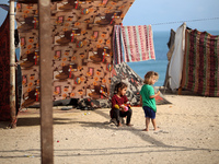 Displaced Palestinians are walking between their tents that they are setting up next to the beach, in Deir el-Balah, central Gaza Strip, on...