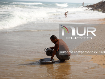 A Palestinian man is washing kitchenware on the beach in Deir el-Balah, central Gaza Strip, on May 26, 2024, amid the ongoing conflict betwe...