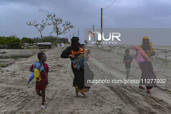 Two women are walking with their child towards a shelter during a rainfall in Kuakata, Bangladesh, on May 26, 2024, ahead of Cyclone Remal's...