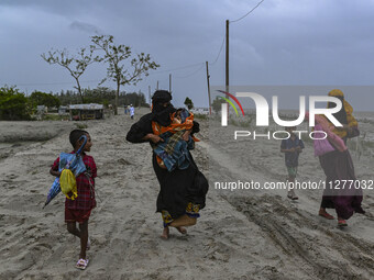 Two women are walking with their child towards a shelter during a rainfall in Kuakata, Bangladesh, on May 26, 2024, ahead of Cyclone Remal's...