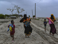 Two women are walking with their child towards a shelter during a rainfall in Kuakata, Bangladesh, on May 26, 2024, ahead of Cyclone Remal's...