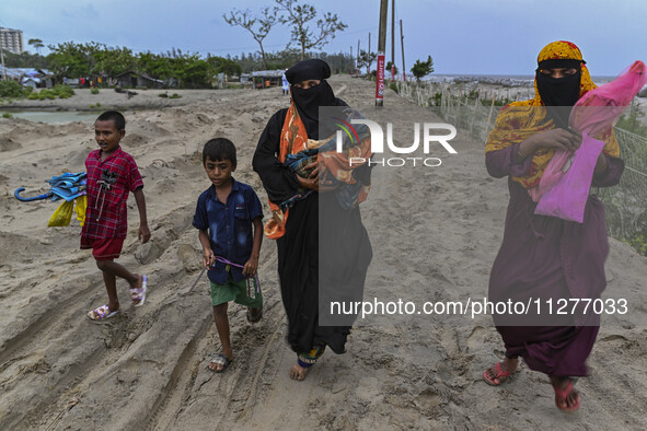 Two women are walking with their child towards a shelter during a rainfall in Kuakata, Bangladesh, on May 26, 2024, ahead of Cyclone Remal's...