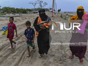 Two women are walking with their child towards a shelter during a rainfall in Kuakata, Bangladesh, on May 26, 2024, ahead of Cyclone Remal's...