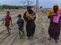 Two women are walking with their child towards a shelter during a rainfall in Kuakata, Bangladesh, on May 26, 2024, ahead of Cyclone Remal's...