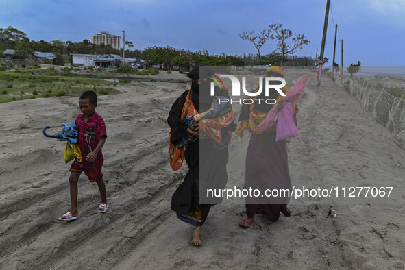 Two women are walking with their child towards a shelter during a rainfall in Kuakata, Bangladesh, on May 26, 2024, ahead of Cyclone Remal's...