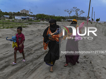 Two women are walking with their child towards a shelter during a rainfall in Kuakata, Bangladesh, on May 26, 2024, ahead of Cyclone Remal's...