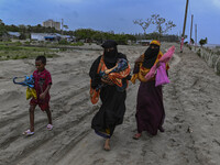 Two women are walking with their child towards a shelter during a rainfall in Kuakata, Bangladesh, on May 26, 2024, ahead of Cyclone Remal's...