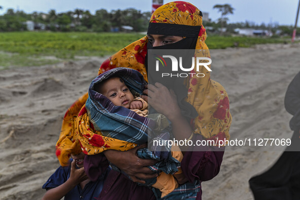 A woman is carrying a child as she is walking towards a shelter during a rainfall in Kuakata, Bangladesh, on May 26, 2024, ahead of cyclone...