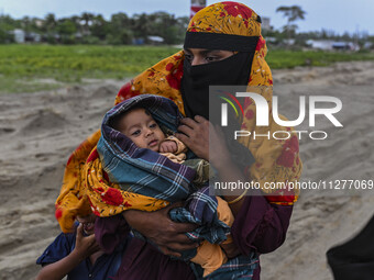 A woman is carrying a child as she is walking towards a shelter during a rainfall in Kuakata, Bangladesh, on May 26, 2024, ahead of cyclone...