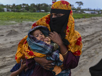 A woman is carrying a child as she is walking towards a shelter during a rainfall in Kuakata, Bangladesh, on May 26, 2024, ahead of cyclone...