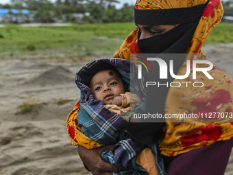 A woman is carrying a child as she is walking towards a shelter during a rainfall in Kuakata, Bangladesh, on May 26, 2024, ahead of cyclone...