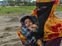 A woman is carrying a child as she is walking towards a shelter during a rainfall in Kuakata, Bangladesh, on May 26, 2024, ahead of cyclone...