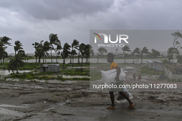 A man is walking with his belongings towards a shelter during a rainfall in Kuakata, Bangladesh, on May 26, 2024, ahead of cyclone Remal's l...