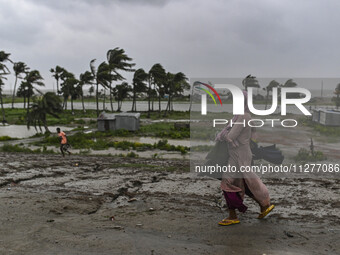 A woman is walking with her belongings towards a shelter during a rainfall in Kuakata, Bangladesh, on May 26, 2024, ahead of cyclone Remal's...