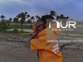 A volunteer is carrying a baby girl to take shelter in the Cyclone Shelter in Kuakata, Bangladesh, on May 26, 2024, ahead of cyclone Remal's...