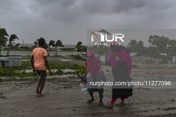 People with their belongings are walking towards a shelter during a rainfall in Kuakata, Bangladesh, on May 26, 2024, ahead of cyclone Remal...