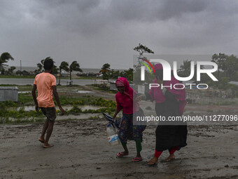 People with their belongings are walking towards a shelter during a rainfall in Kuakata, Bangladesh, on May 26, 2024, ahead of cyclone Remal...